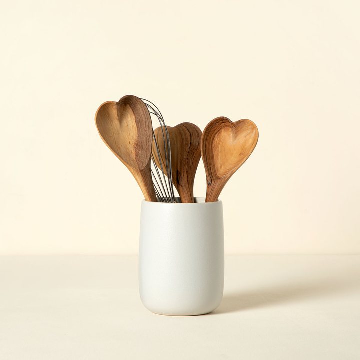 Heart-shaped olive wood serving spoons standing in a pale ceramic crock