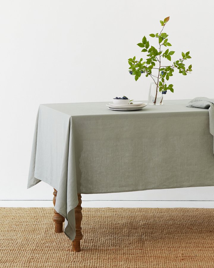 Sage green linen tablecloth on a wooden table with a sprig of blueberry branches